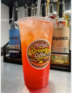 Orange drink in a cup with 'Milly's Groovy Coffee' label, surrounded by bottles on a metallic surface.